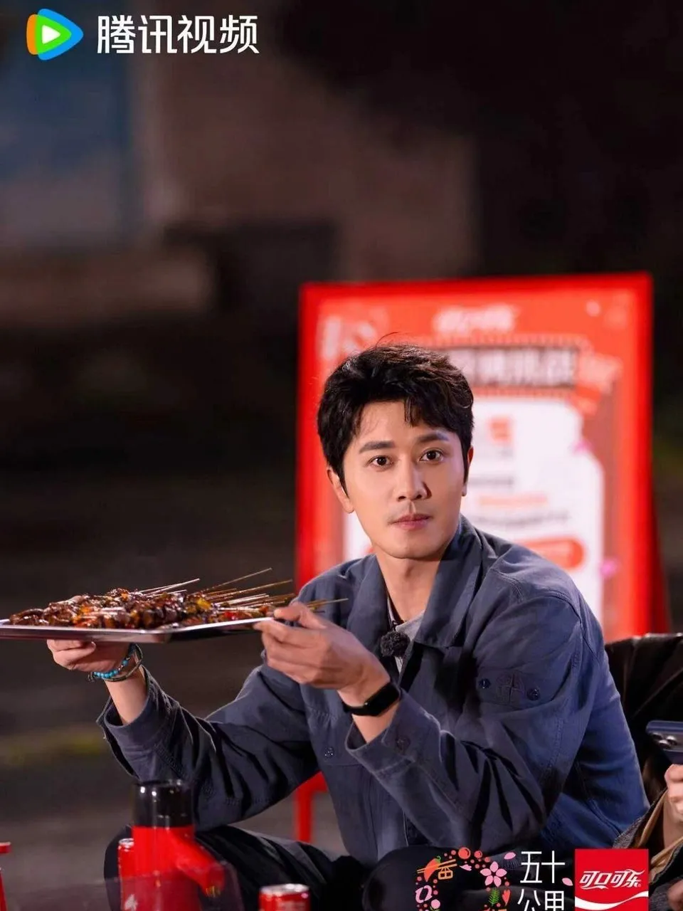 A man holds a tray of grilled meat skewers at a table.