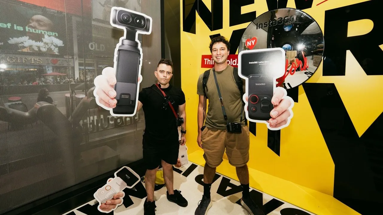 Two men stand beside oversized cutouts of handheld 360-degree cameras at a yellow Insta360 display.