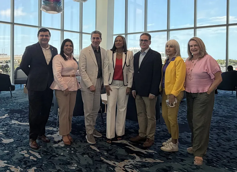 Seven business professionals stand together in a windowed meeting room.