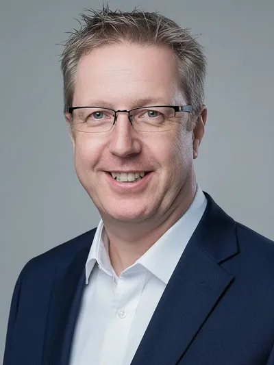 Bjorn Vikard smiling in glasses, a navy suit jacket and white shirt against a gray background.
