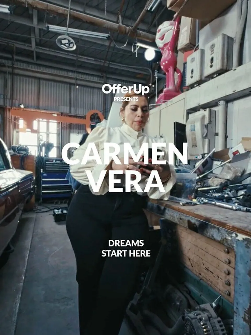 Carmen Vera in a garage beside a workbench covered with tools and car parts.