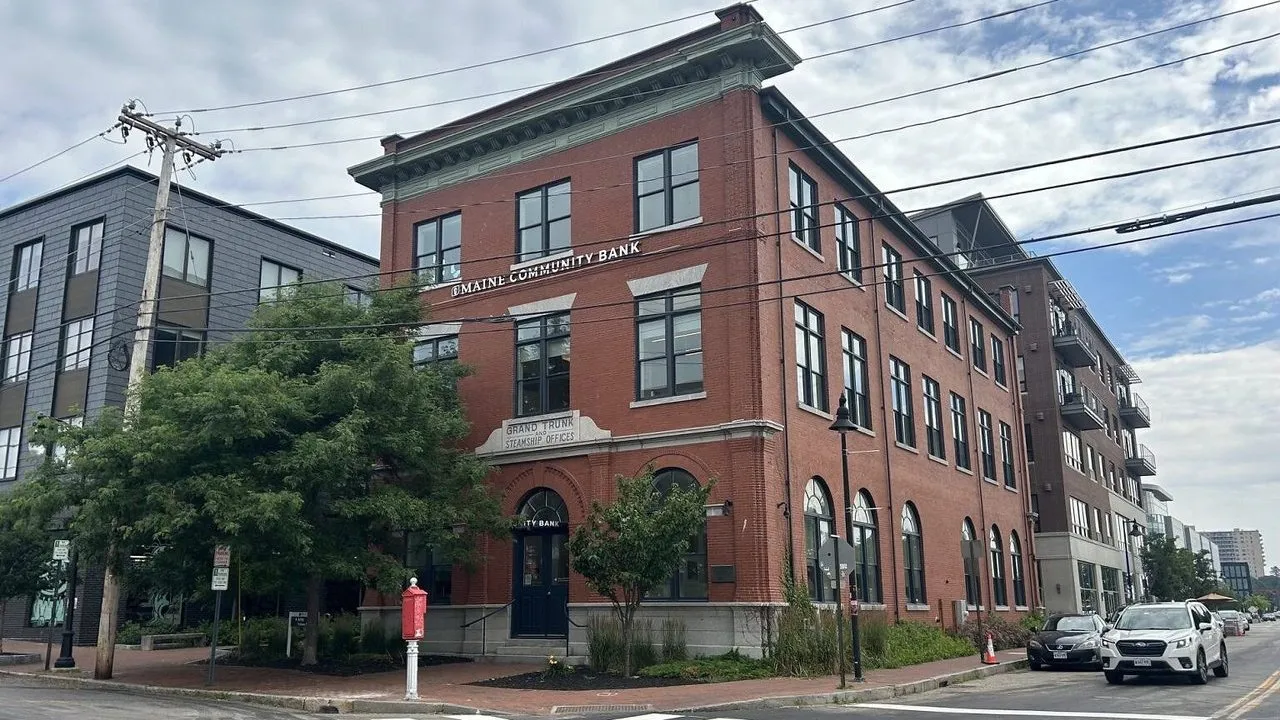 Maine Community Bank in a red brick building on a city street with parked cars.