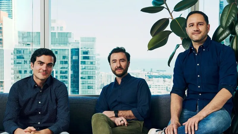 Three people seated in an office with city views and a large leafy plant.