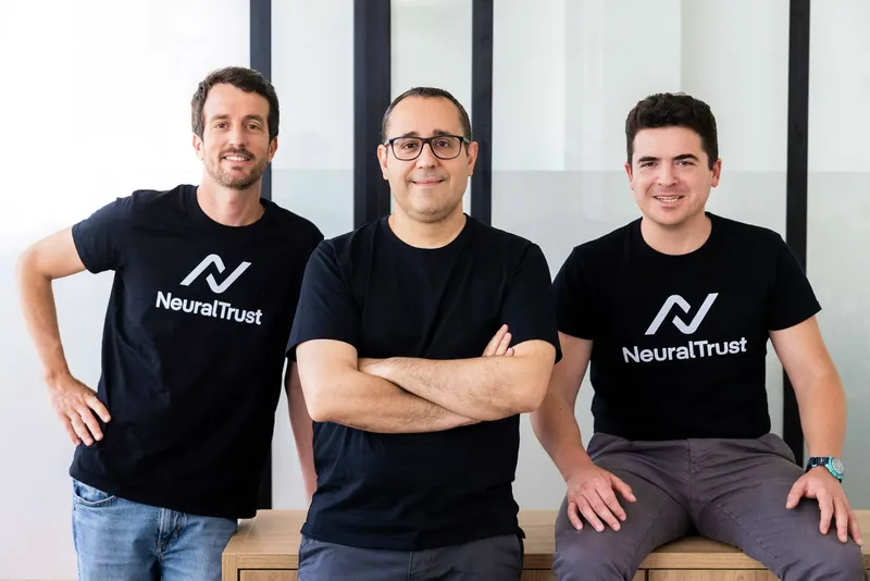 Three NeuralTrust founders wearing black shirts, standing and sitting in an office.