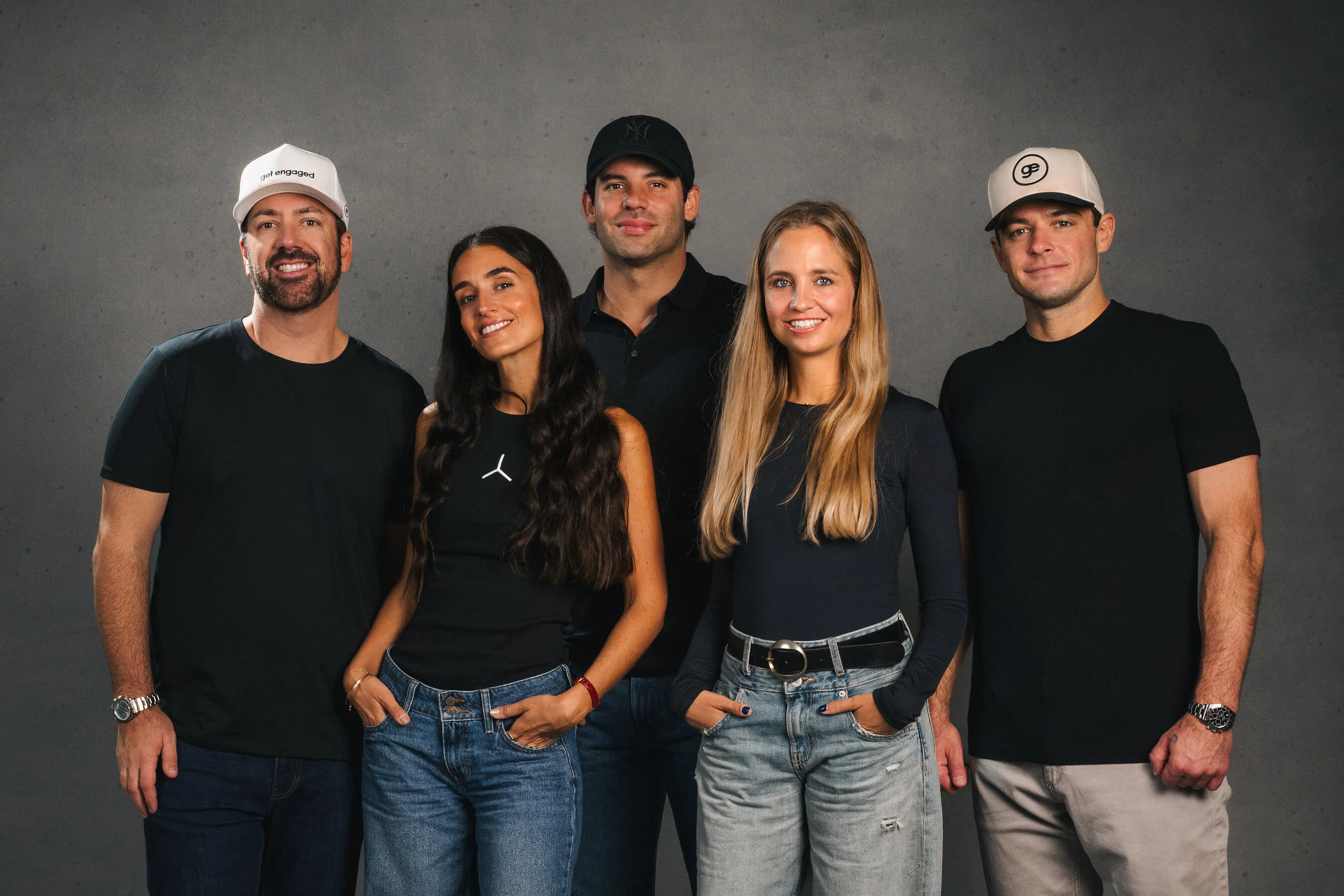 Five people in black tops standing against a grey wall.