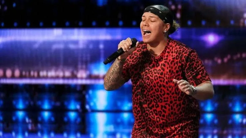 Celina Graves sings into a microphone on a blue-lit stage, wearing a red leopard-print shirt.