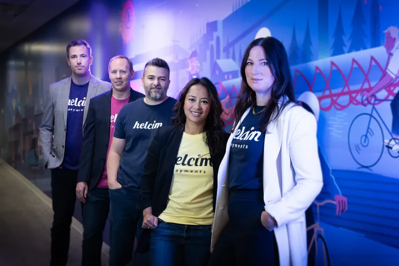 Five Helcim employees standing in front of a colorful mural.