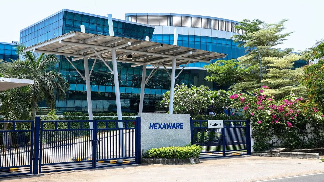 Hexaware office entrance with blue glass facade, gate and landscaped trees and flowering shrubs