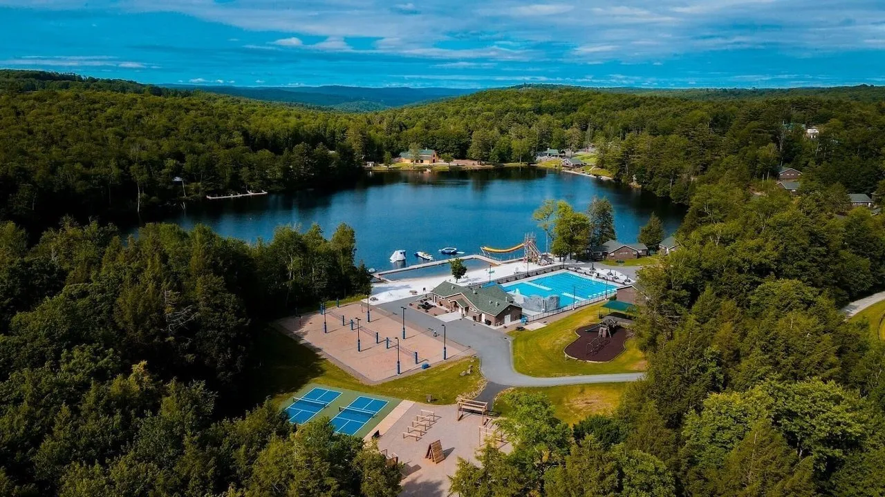 A lakeside recreation area with a pool, tennis courts, playground and docks surrounded by forest