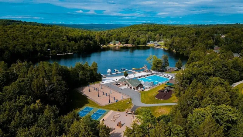 A lakeside recreation area with a pool, tennis courts, playground and docks surrounded by forest