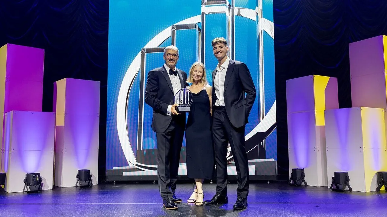 John Magee, center, with two people holding an award onstage at a ceremony