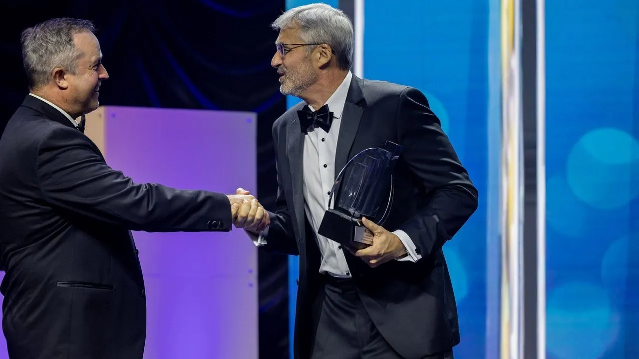 John Magee accepts an EY EOY award while shaking hands with another man.