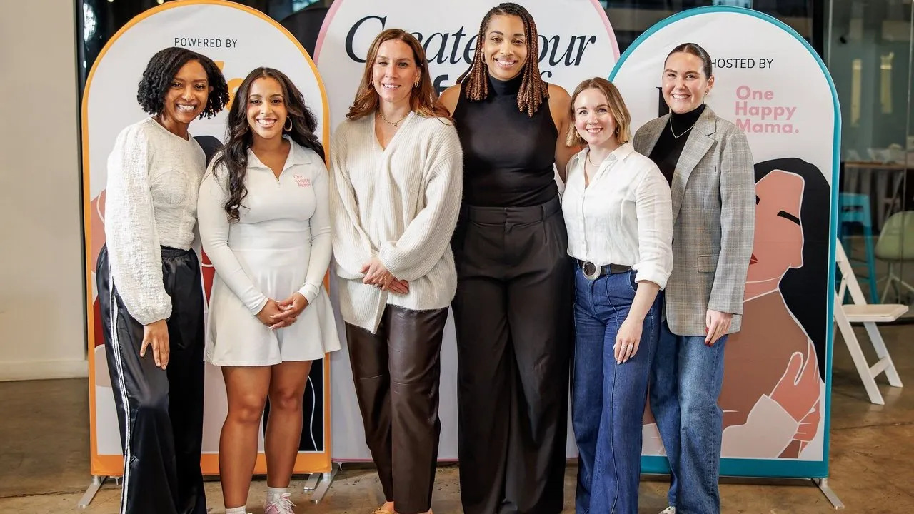 Six women stand in front of event banners reading “Create Your” and “One Happy Mama.”