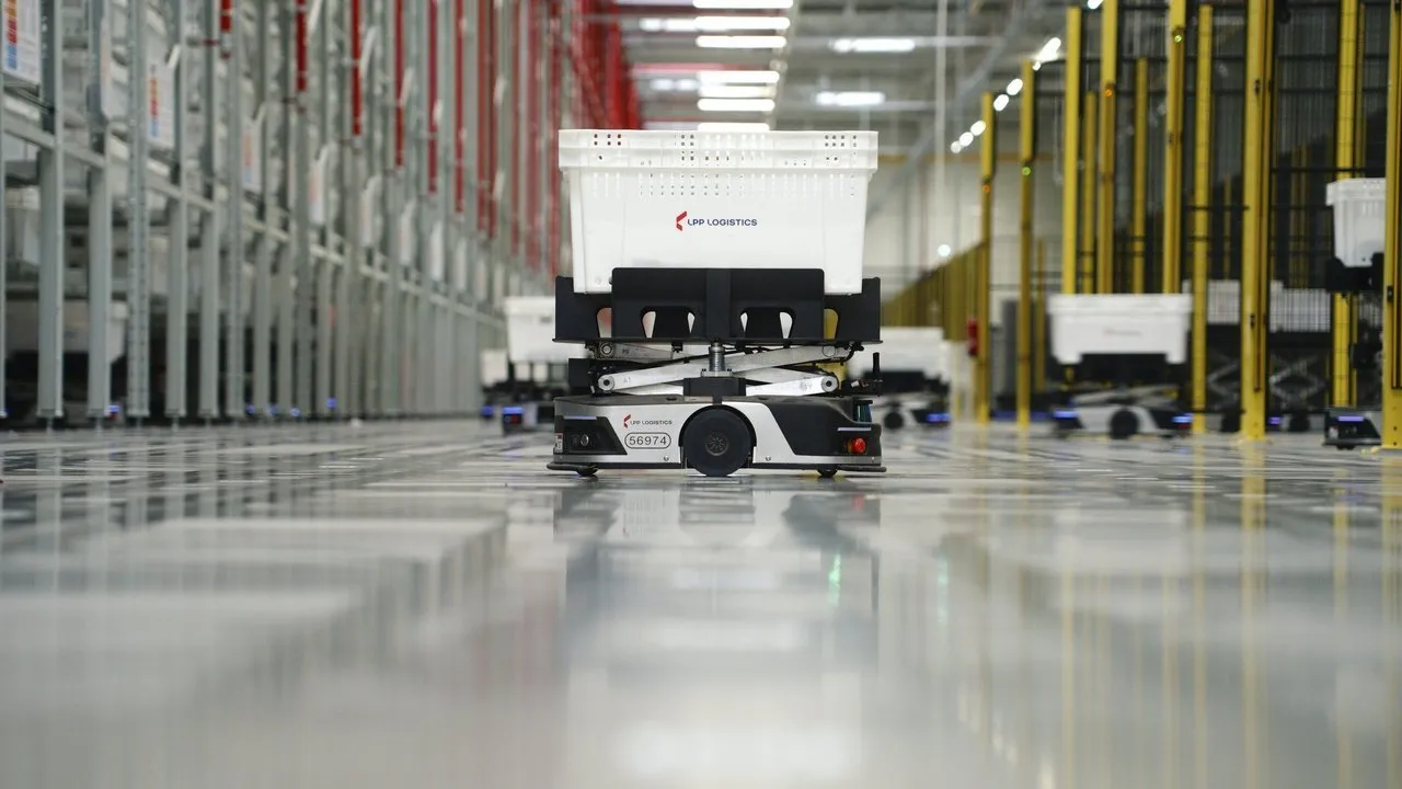 Autonomous warehouse robot carrying a white plastic crate between storage racks