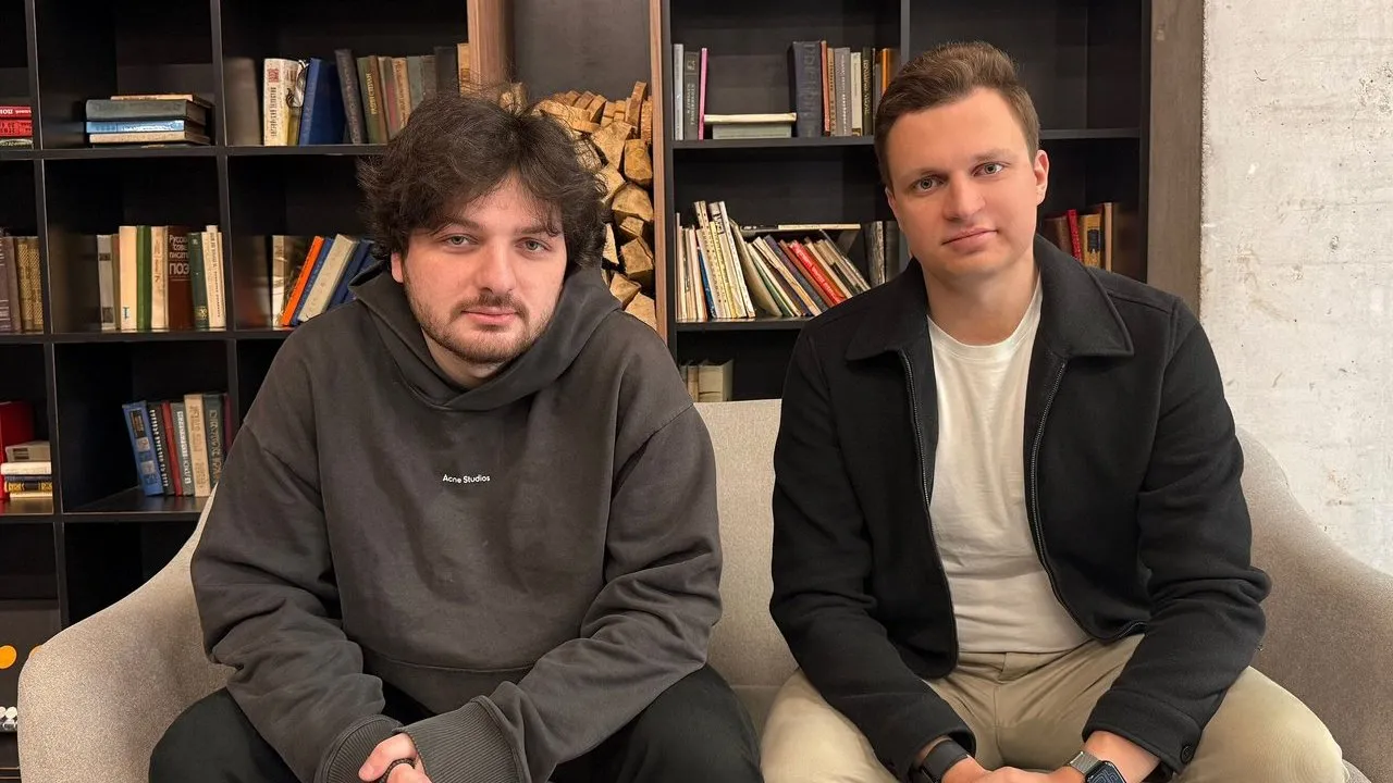 Levan Kvirkvelia and Daniel Dhawan seated on a sofa in front of bookshelves.