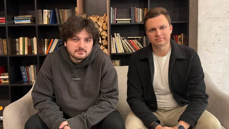 Levan Kvirkvelia and Daniel Dhawan seated on a sofa in front of bookshelves.