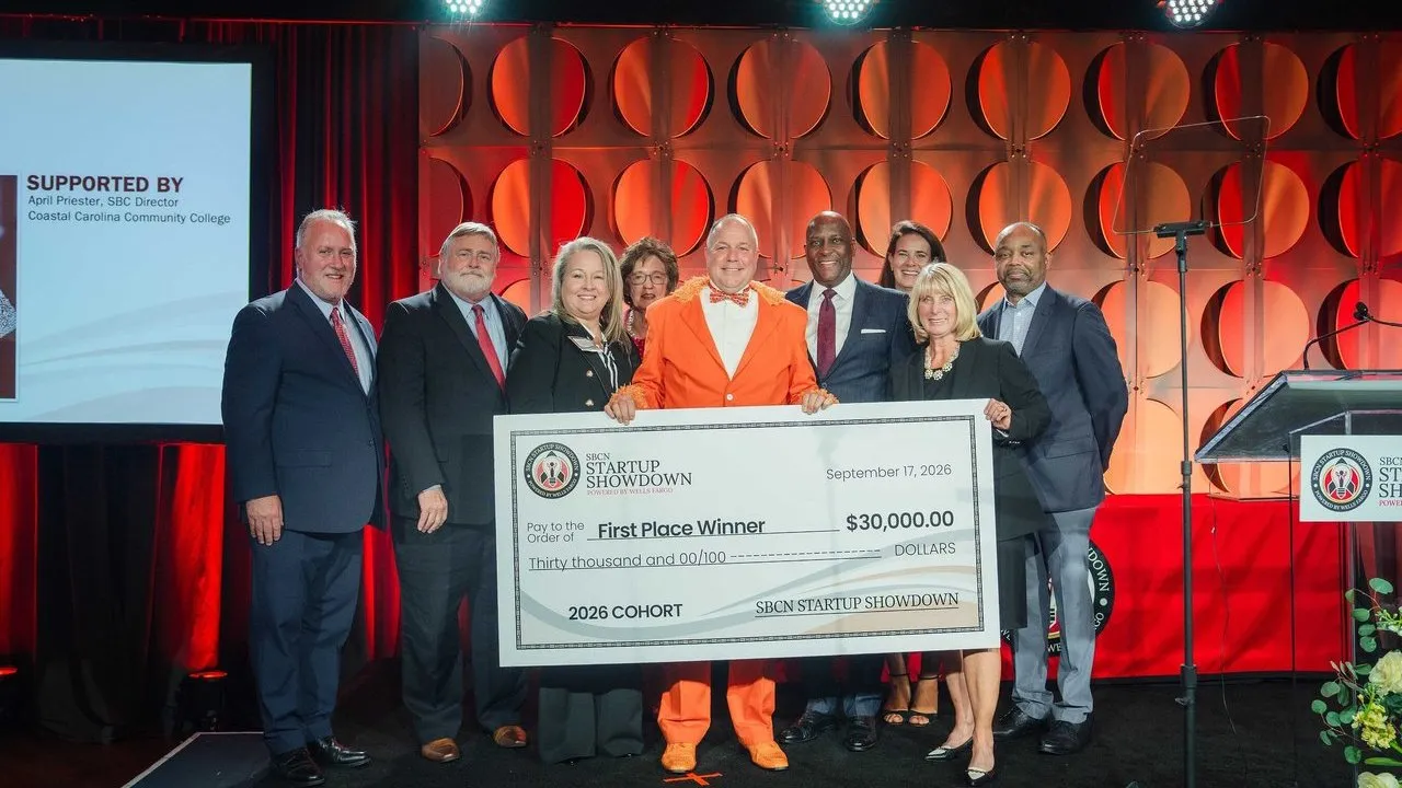 Eight officials stand with a winner holding a $30,000 Startup Showdown check onstage.