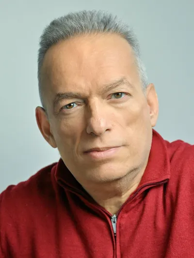 Paris Petrou in a red zip-up sweater against a pale blue background.
