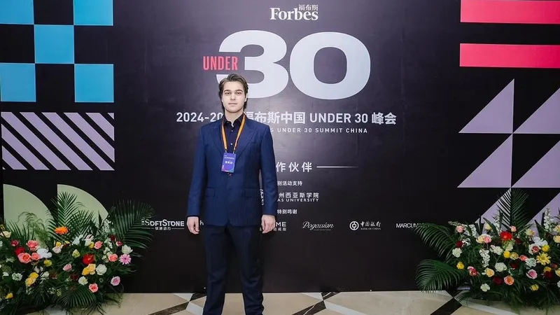 A man in a navy suit stands before a Forbes Under 30 China summit backdrop with floral arrangements.