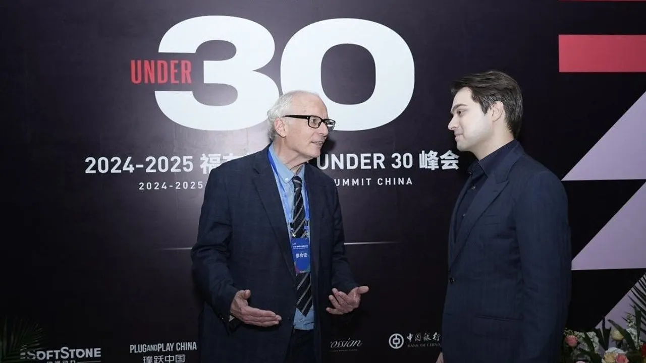Two men in suits talk before an Under 30 Summit China backdrop.