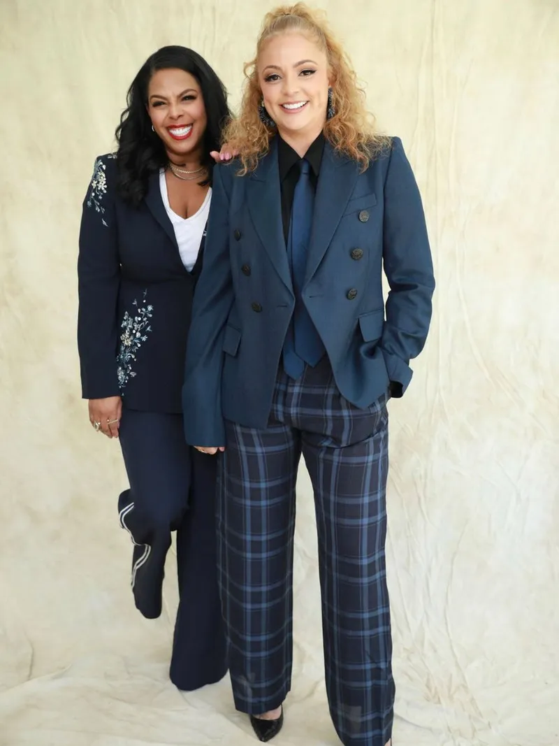 Dia Simms and Erin J Hall smiling in navy suits against a cream backdrop.