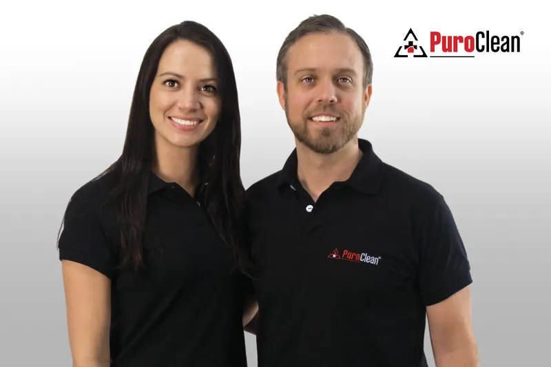 Two people in black PuroClean shirts standing beneath a PuroClean logo.