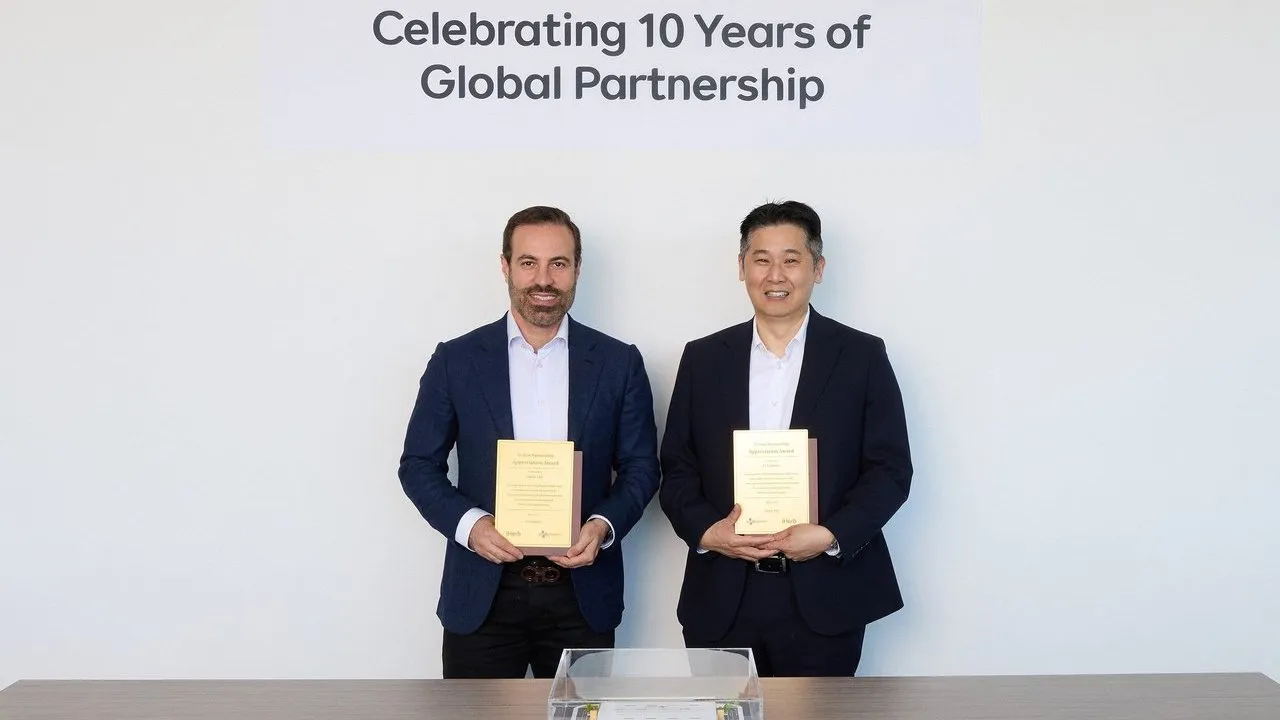Two men hold appreciation awards beneath a sign reading “Celebrating 10 Years of Global Partnership.”