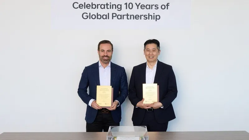 Two men hold appreciation awards beneath a sign reading “Celebrating 10 Years of Global Partnership.”