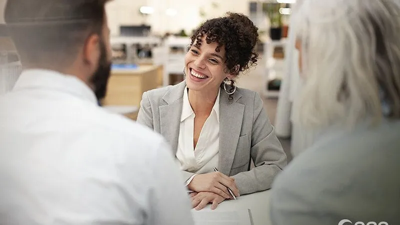 Bank adviser smiling as she speaks with two customers across a desk.