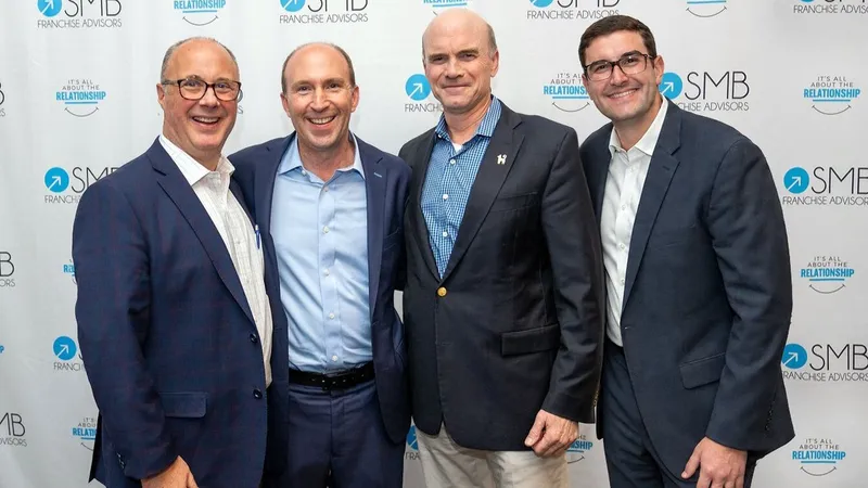 Four men in business suits pose before an SMB Franchise Advisors backdrop.
