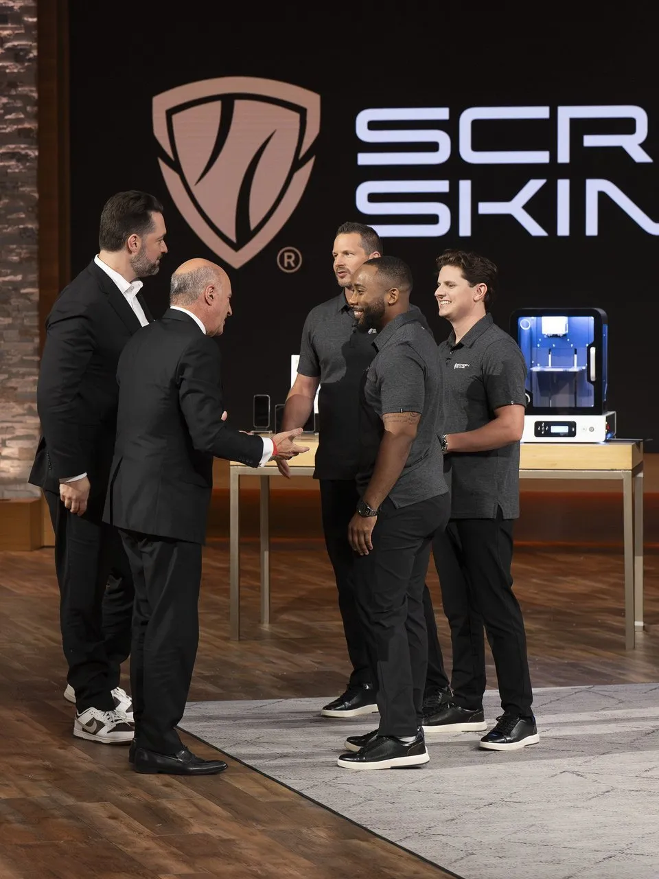 Five men stand beside a Screen Skinz machine in front of a large Screen Skinz logo.