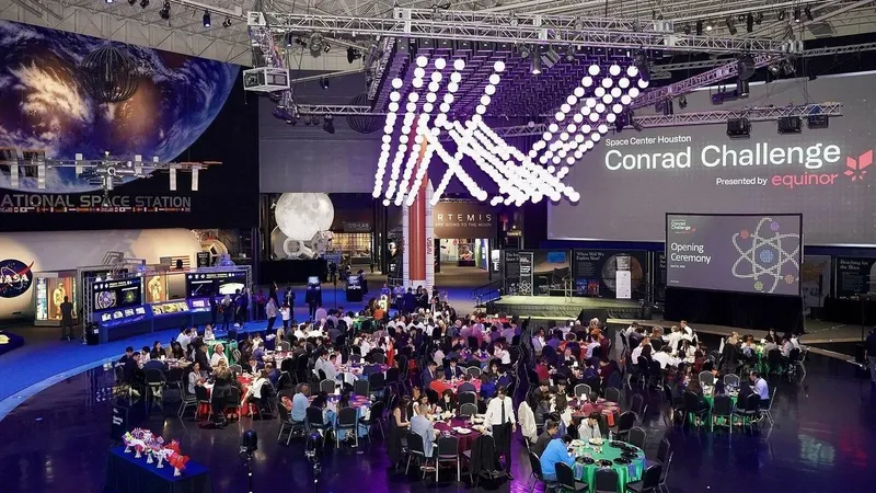 Guests seated at banquet tables beneath a space station exhibit and Conrad Challenge stage.