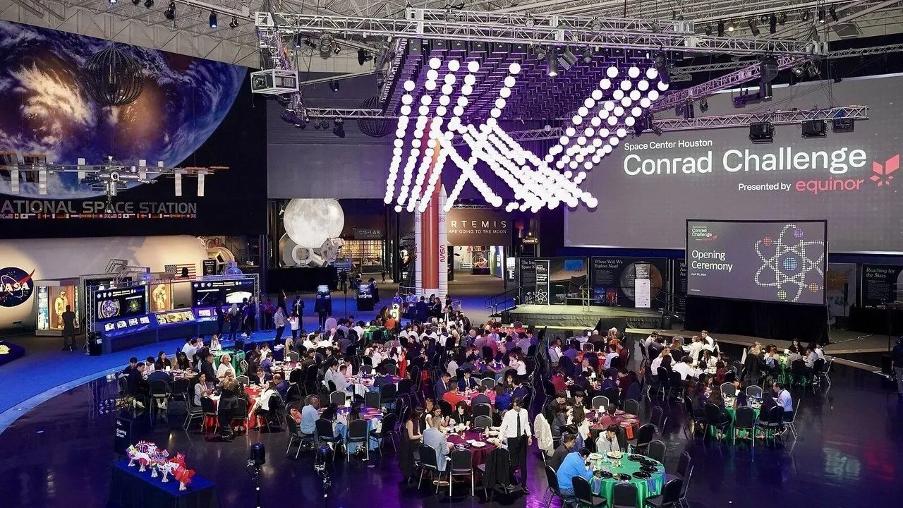Guests seated at banquet tables beneath a space station exhibit and Conrad Challenge stage.
