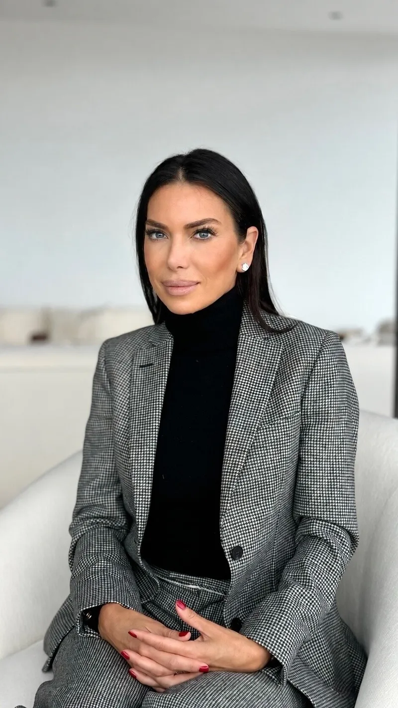 Tanya Zuckerbrot in a black turtleneck and checked blazer, seated on a white chair.