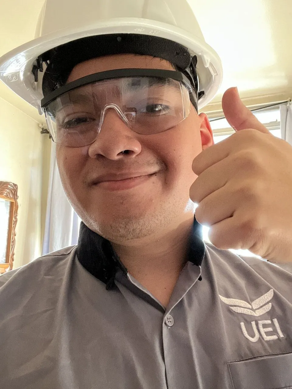 UEI College student in a hard hat and safety glasses gives a thumbs-up.