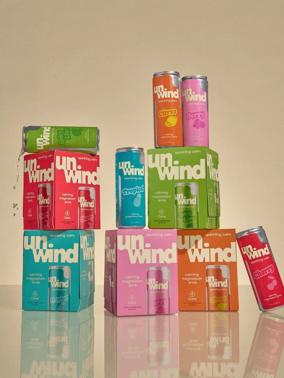 Colorful Unwind sparkling calm drink cans and four-packs arranged on a reflective surface.
