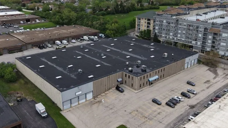 A large industrial warehouse with loading bays, parked vehicles and surrounding commercial buildings