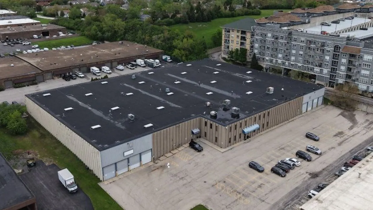A large industrial warehouse with loading bays, parked vehicles and surrounding commercial buildings
