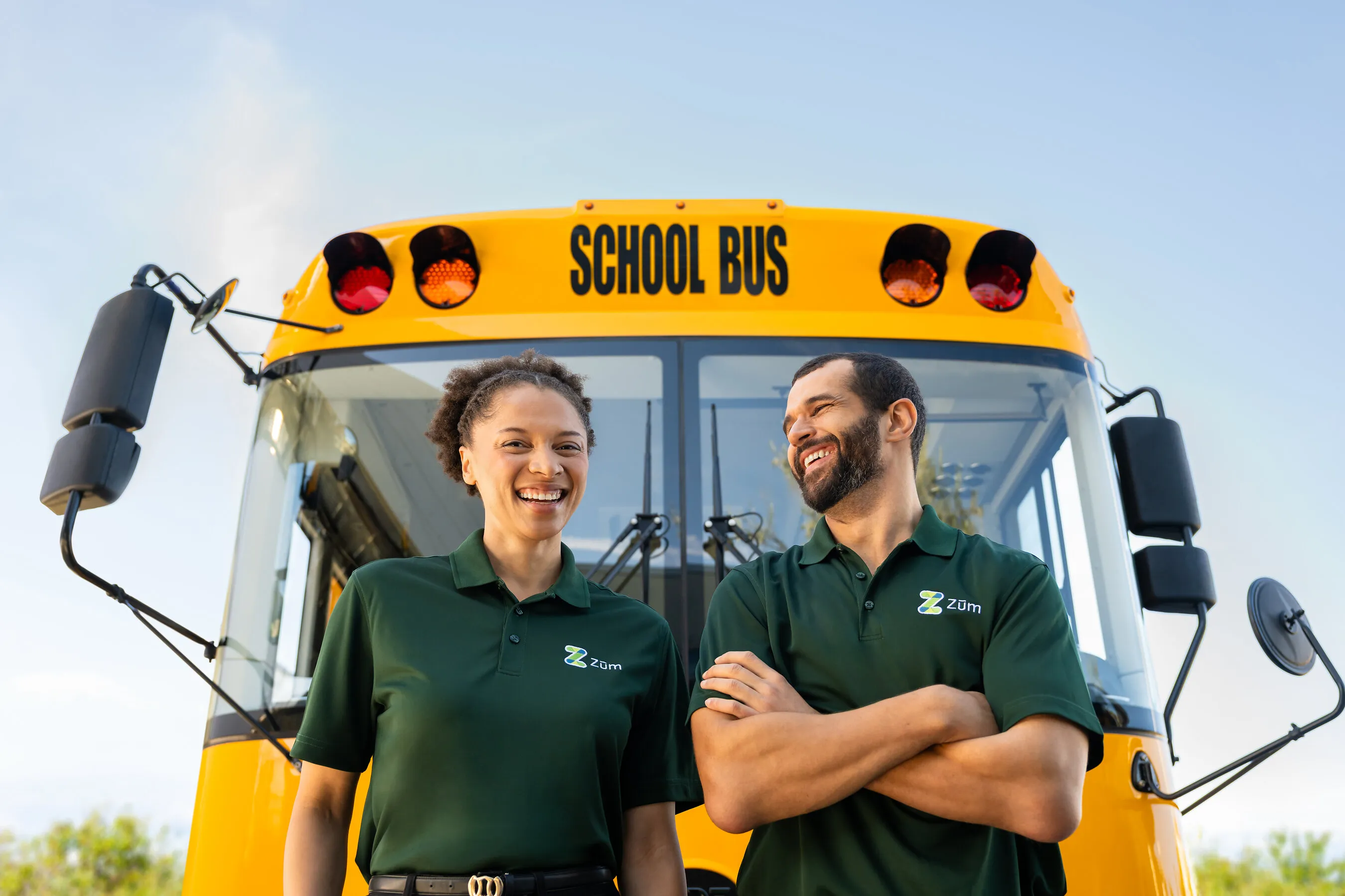 Two school bus staff members standing in front of a yellow school bus.