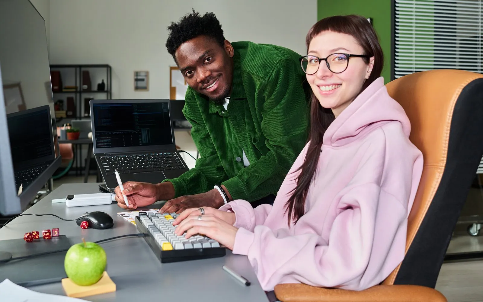 Two young interns smiling at their computer in a tech office