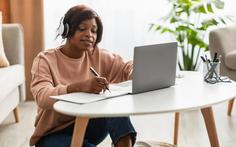 A woman with headphones taking notes during an online course