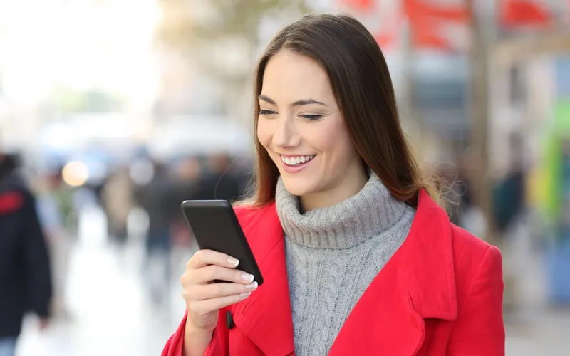 A woman in a red winter coat smiling at her phone