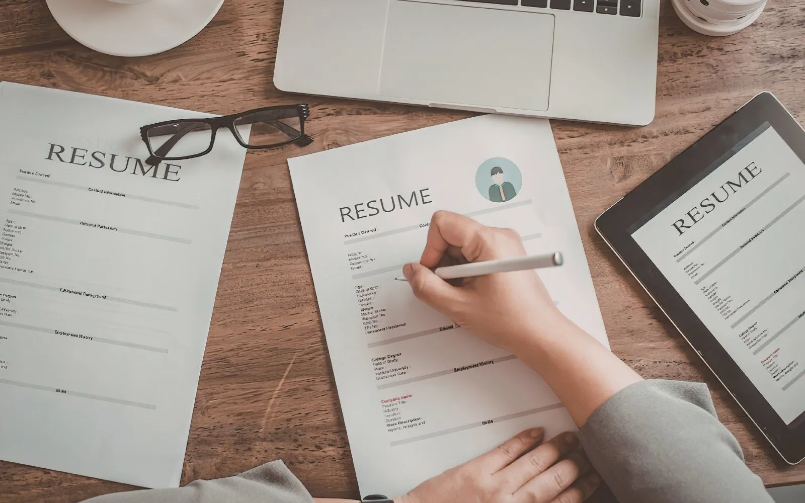 A hand filling in a CV beside printed résumés