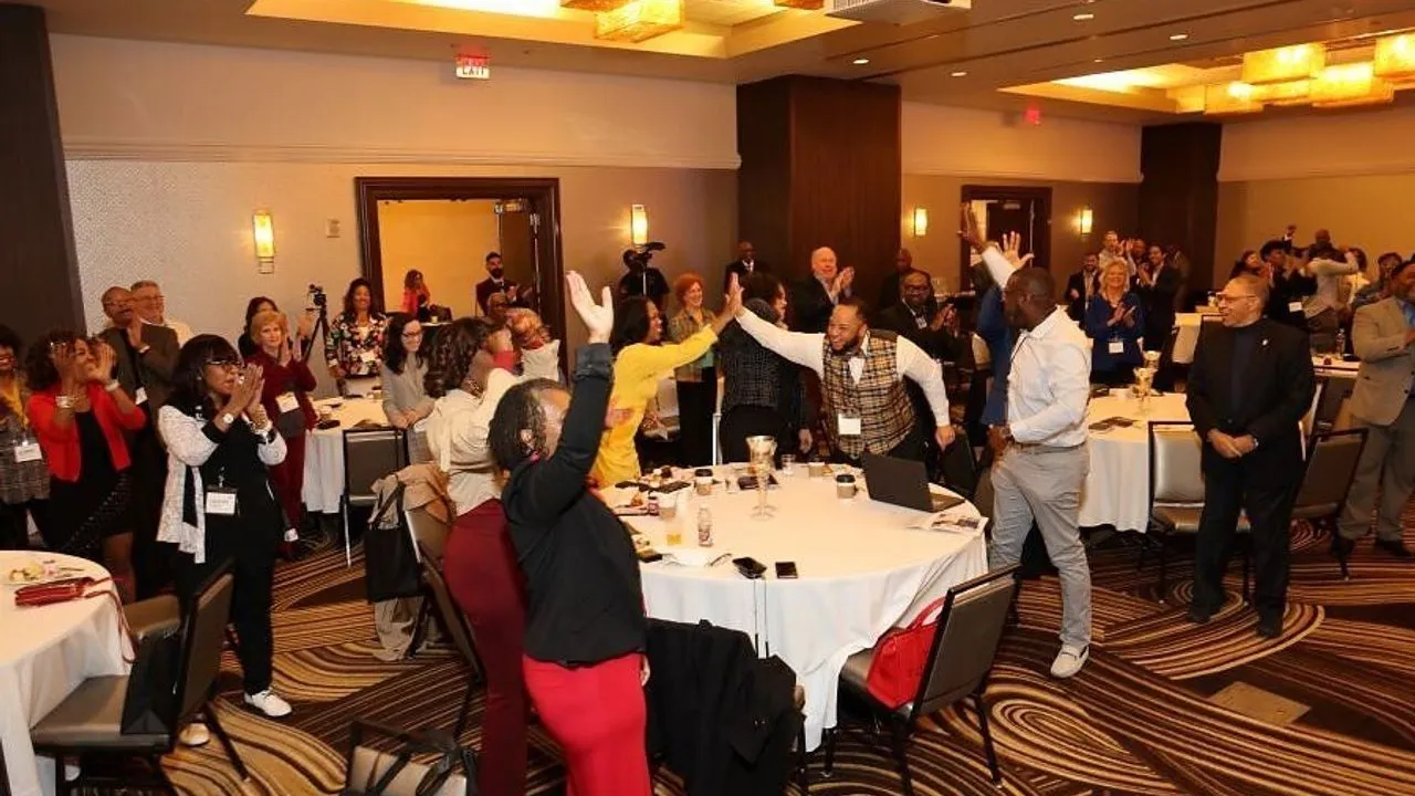 Attendees at tables raise their hands and applaud during a conference.