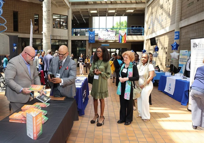 People queue at a book table during an indoor community event.