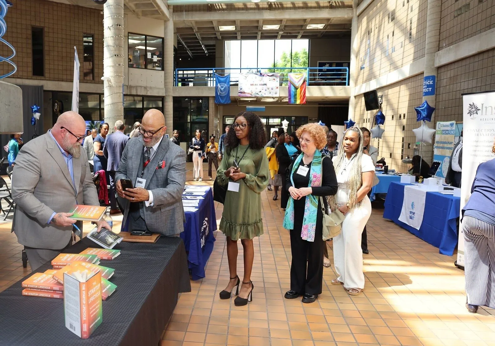 People queue at a book table during an indoor community event.