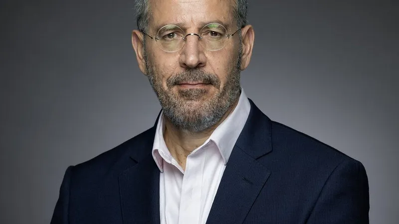 ABnet CEO Shimon Amouyal in a dark suit and glasses against a gray background.