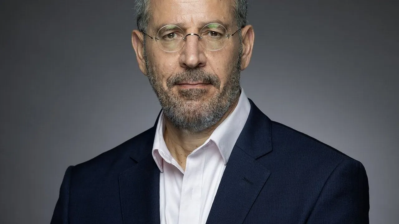 ABnet CEO Shimon Amouyal in a dark suit and glasses against a gray background.