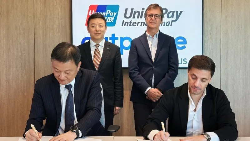 Two men sign documents as two others stand before a UnionPay International sign.