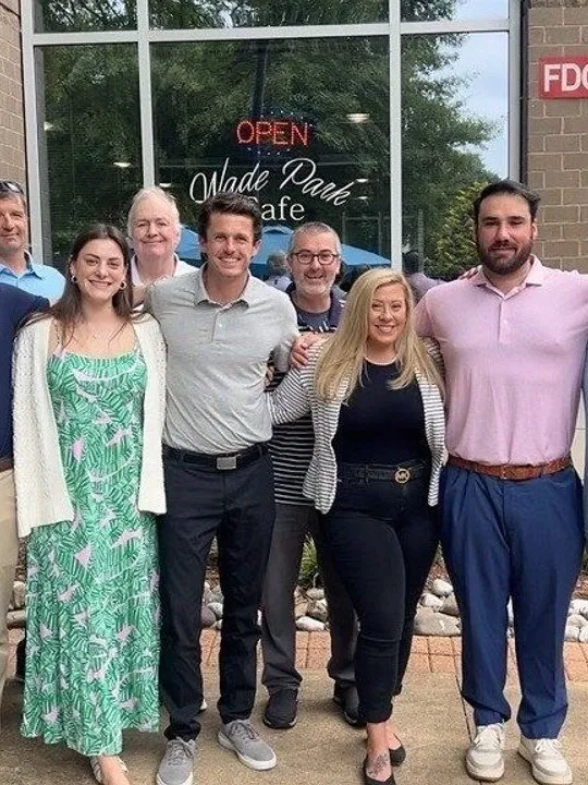 Ten adults pose outside Made Paris Cafe beneath an open sign.